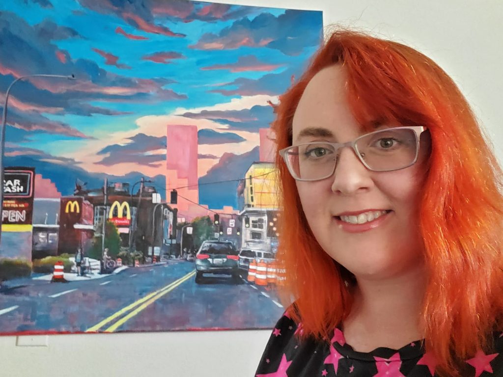 A picture of Willow D'Arcy in front of a cityscape painting.